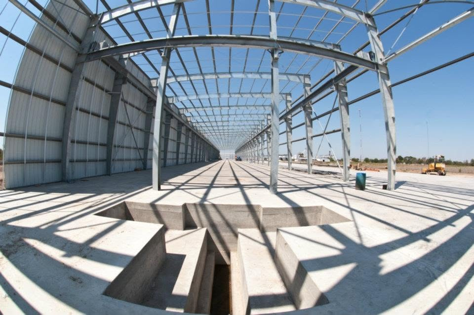 Interior of a large steel-frame warehouse structure under construction with concrete floor channels