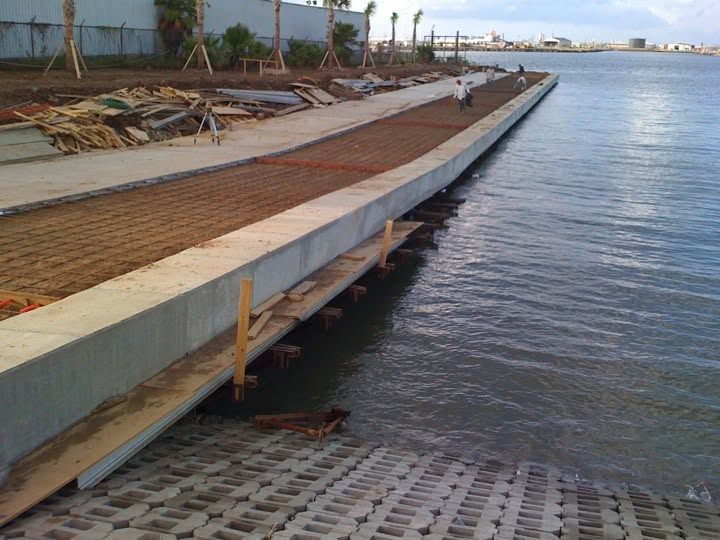 Waterfront concrete dock under construction with rebar and workers along the water